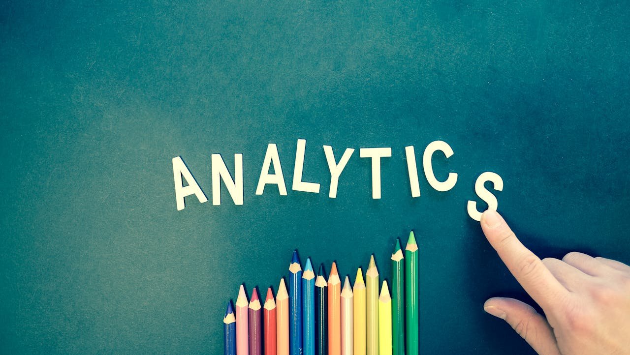 about-01 Colored pencils and letters spelling ANALYTICS on a textured background with a hand.