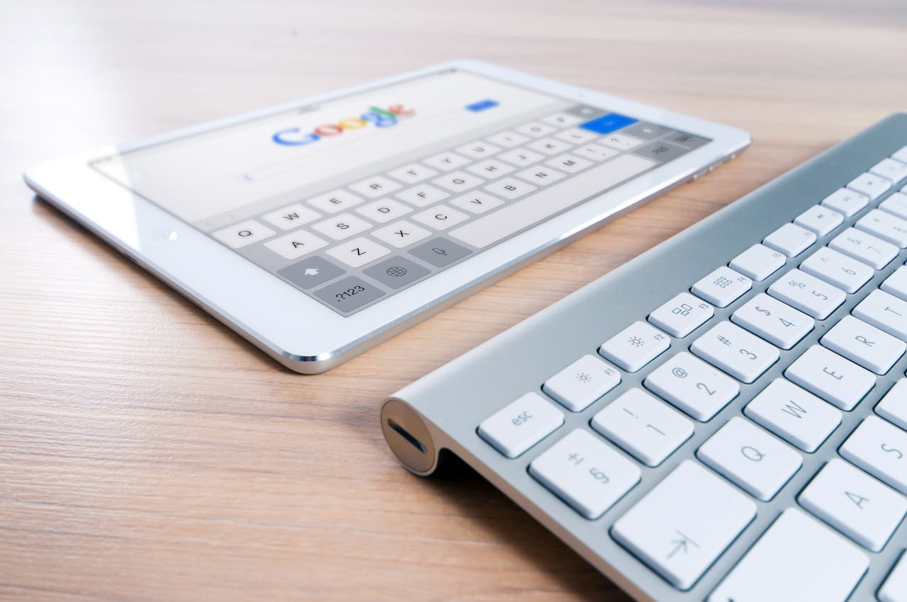 services-01 A modern tablet displaying a search engine logo next to a wireless keyboard on a wooden desk.